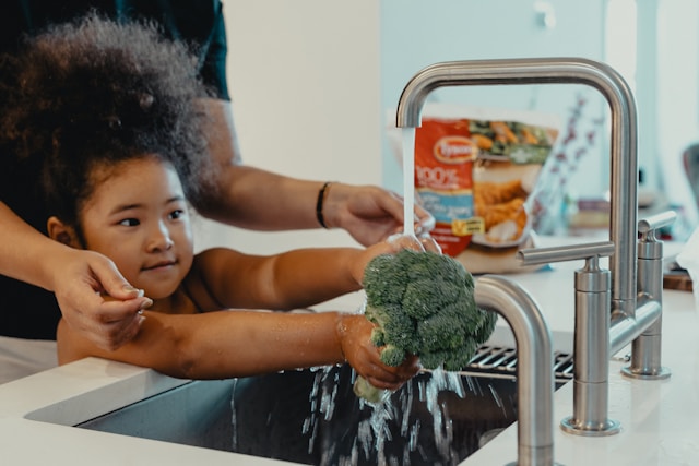 Petite fille passant un légume sous l'eau du robinet, dans la cuisine - consommation de l'eau dans la maison