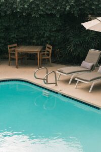Piscine estivale avec transats, parasol et coin repas, entourée de végétation luxuriante, symbole de vacances et de détente au soleil.