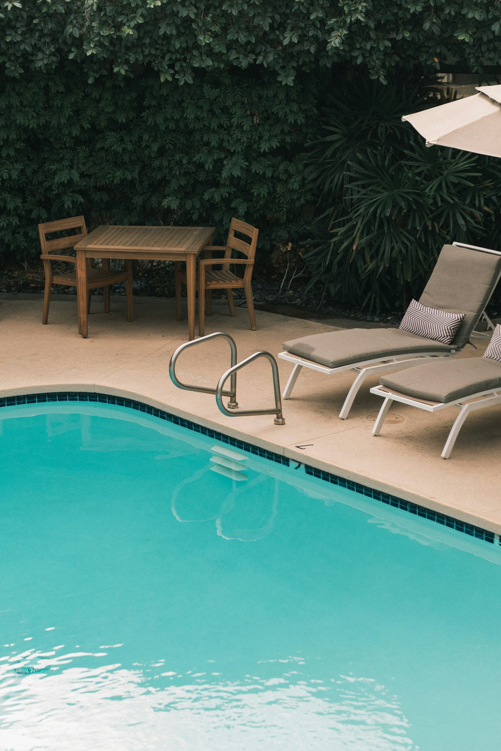Piscine estivale avec transats, parasol et coin repas, entourée de végétation luxuriante, symbole de vacances et de détente au soleil.
