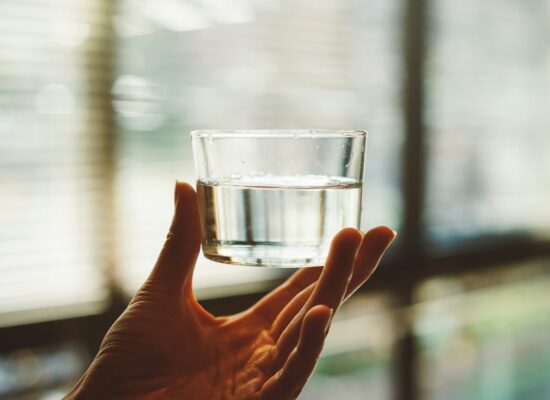 Image de verre d'eau dans une main, mettant en avant la pureté et la clarté de l’eau.